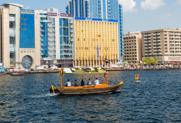 Traditional wooden abra boat ferrying passengers across the Dubai Creek with a backdrop of modern buildings, highlighting the contrast between Dubai's cultural heritage and urban development.
