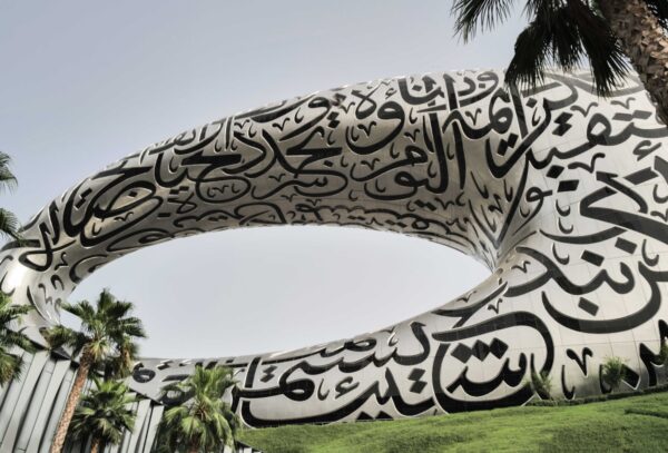 An artistic close-up of the Museum of the Future, showcasing the intricate Arabic calligraphy designs on its facade, with palm trees and a clear sky in the background.