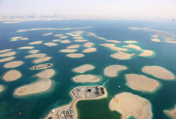 Aerial view of the World Islands in Dubai, with the artificial archipelago's sandbanks resembling a world map, set against the backdrop of the Dubai skyline in the hazy distance.