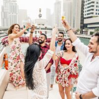 Group of friends celebrating with champagne on a boat in Dubai Marina with skyscrapers in the background.